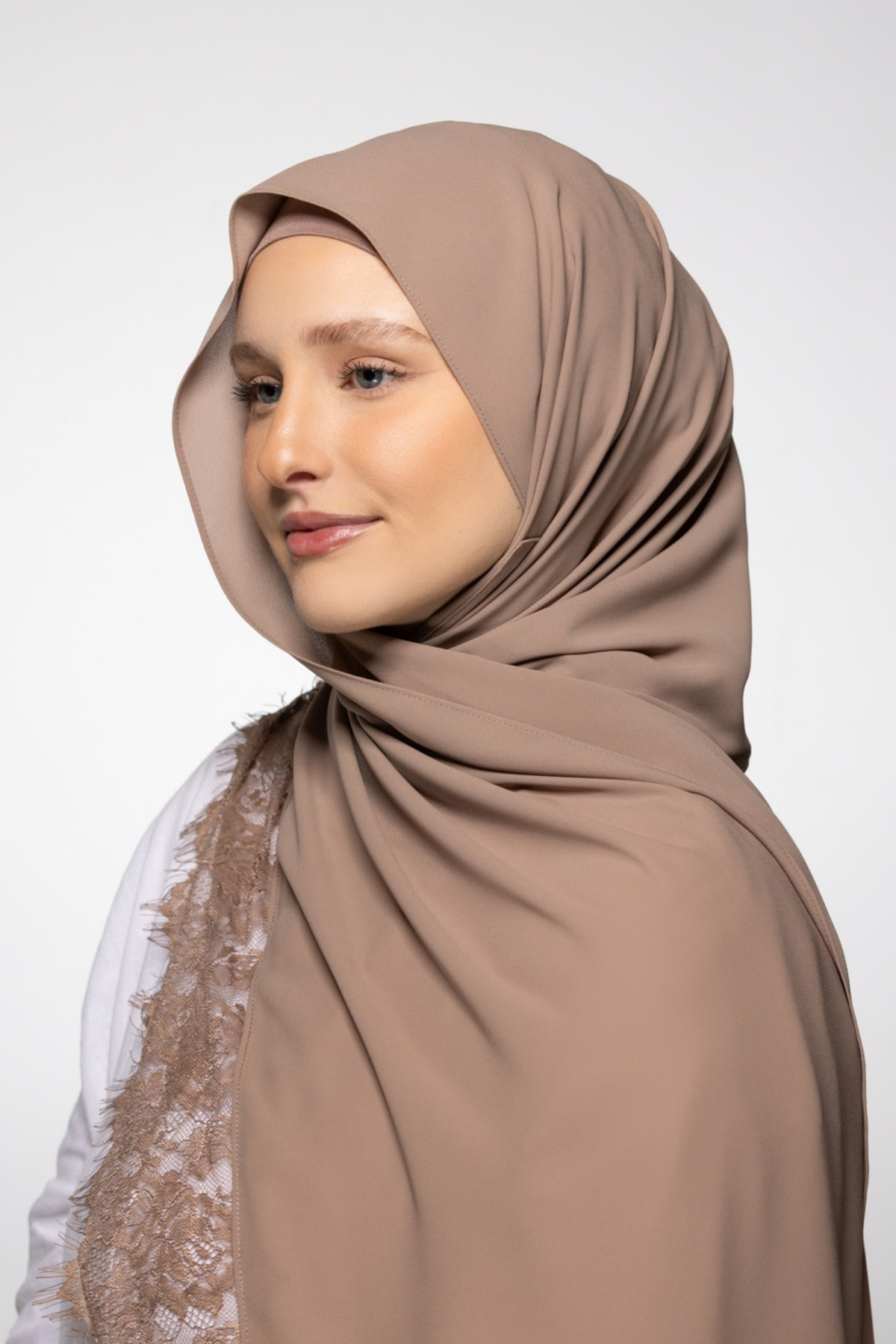 A woman wearing a draped taupe-brown hijab, shown in profile against a light gray studio background.